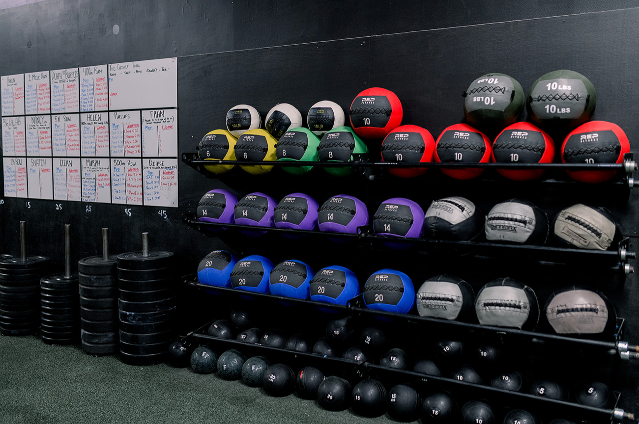 A bunch of medicine balls are sitting on a shelf in a gym.