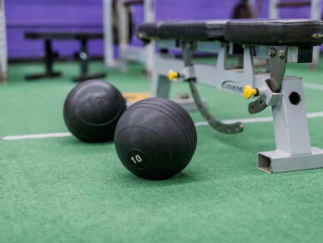 Two medicine balls are sitting on the floor next to a bench in a gym.