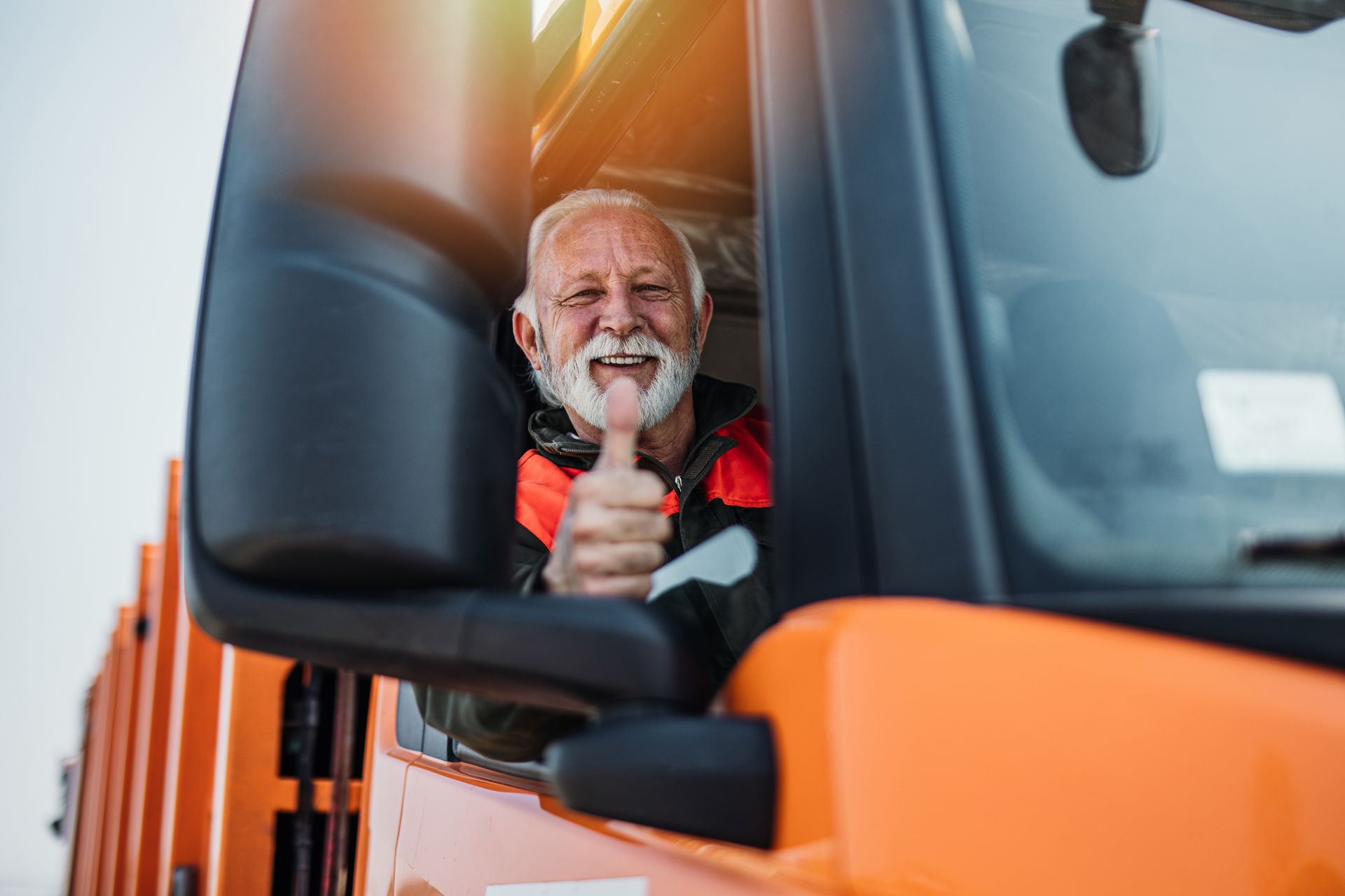 Truck driver gives a thumbs-up from an orange service truck cab.