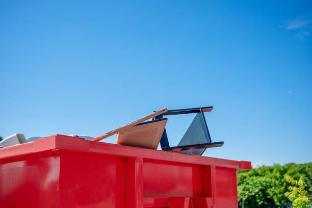 Close-up of a red dumpster filled with furniture and other items set against a clear blue sky