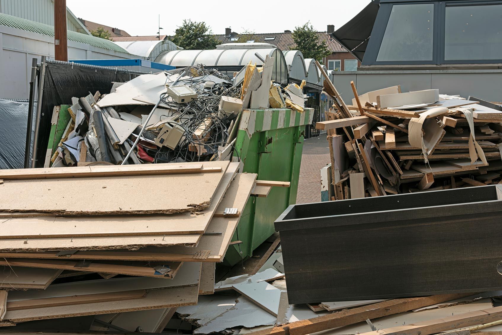 Green dumpster and piles of construction debris at an outdoor site. Green dumpster and piles of construction debris at an outdoor site.