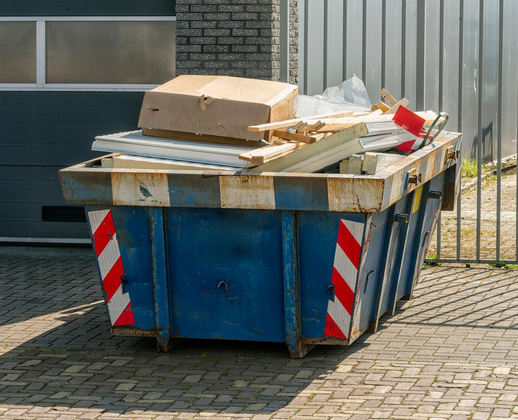 Blue dumpster filled with construction debris and cardboard outdoors.