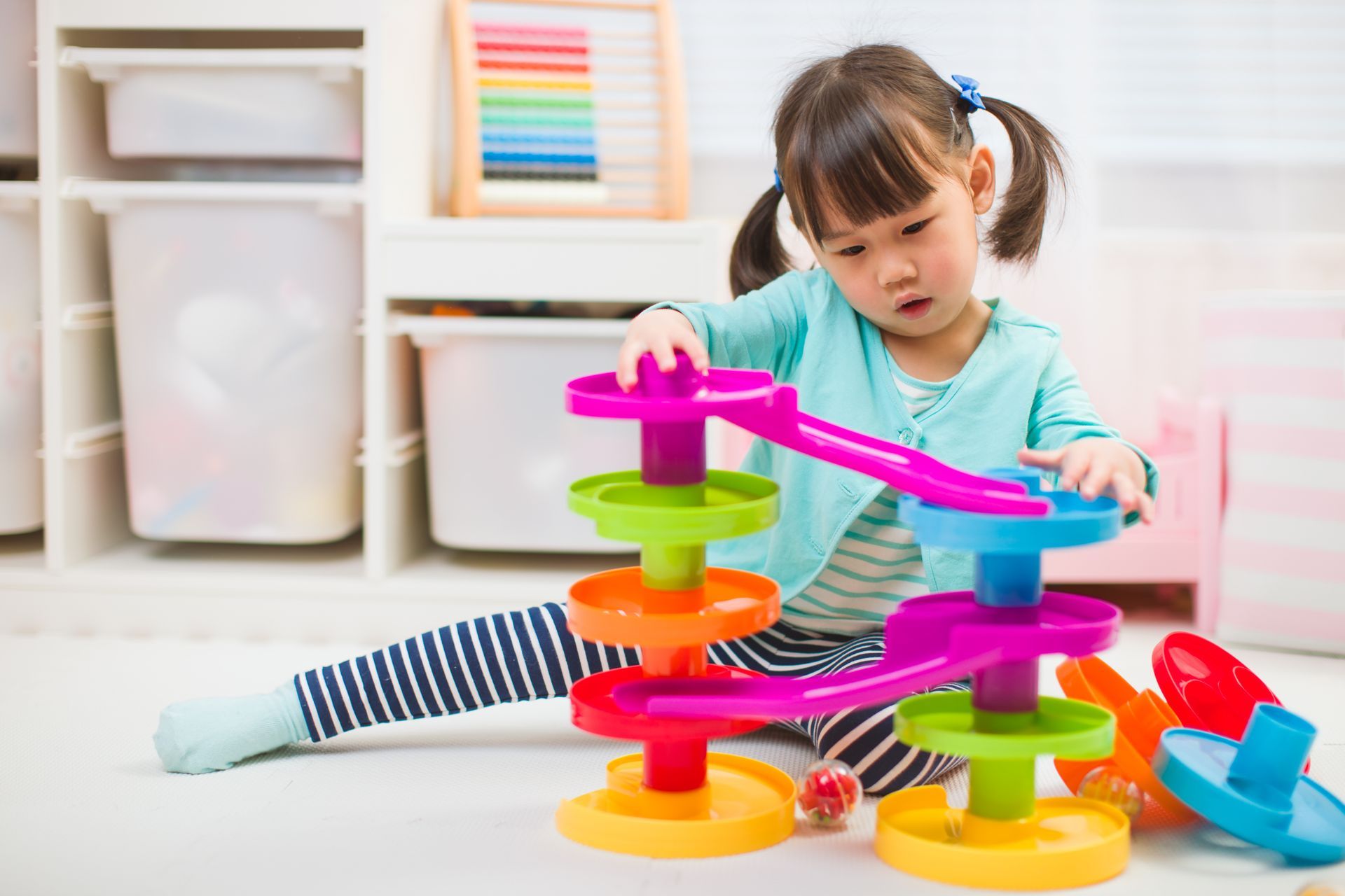 A little girl is playing with a colorful toy on the floor.