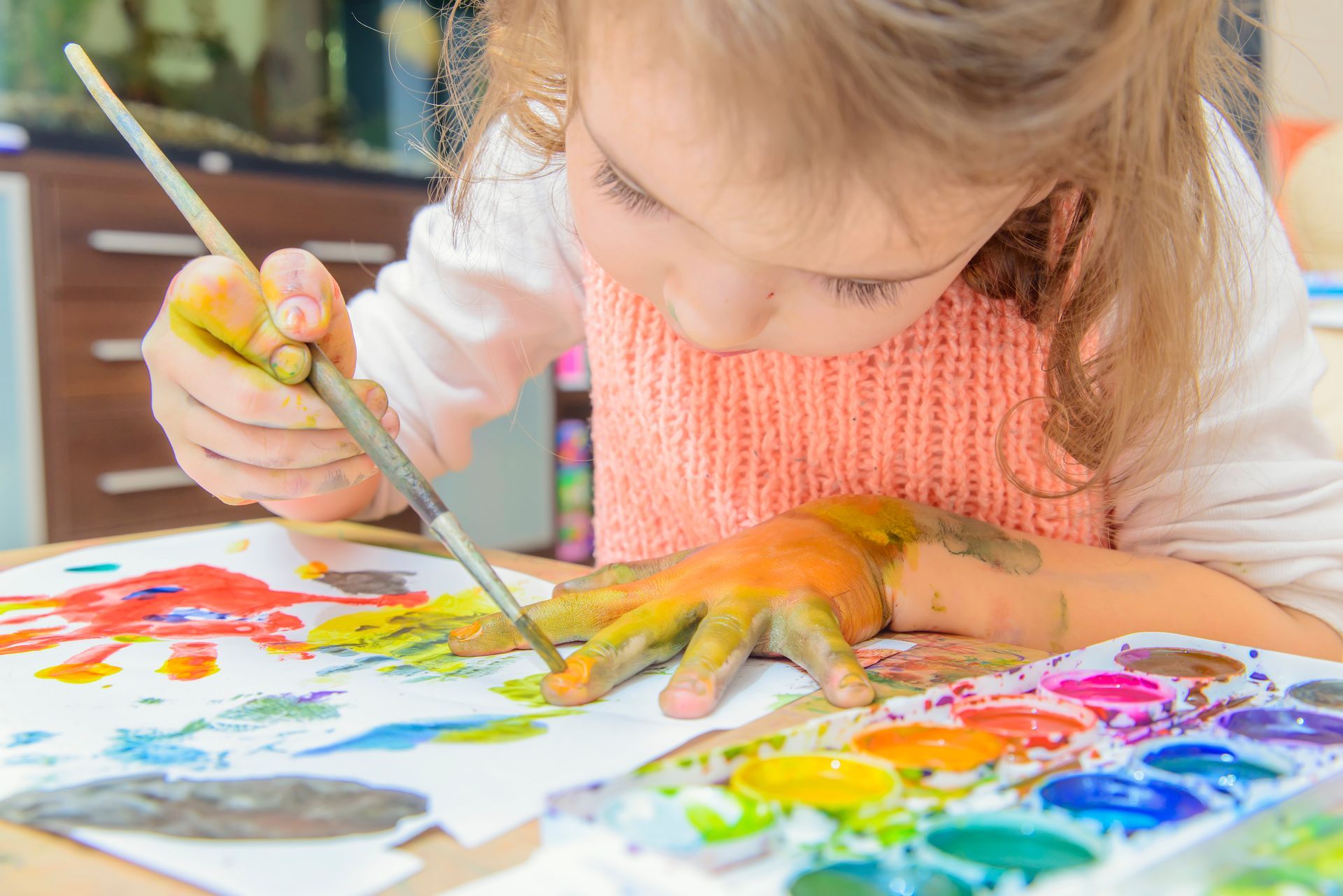 A little girl is painting with her hands on a piece of paper.