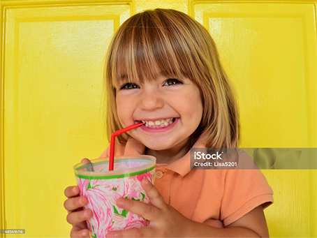 A little girl is drinking from a cup with a straw.