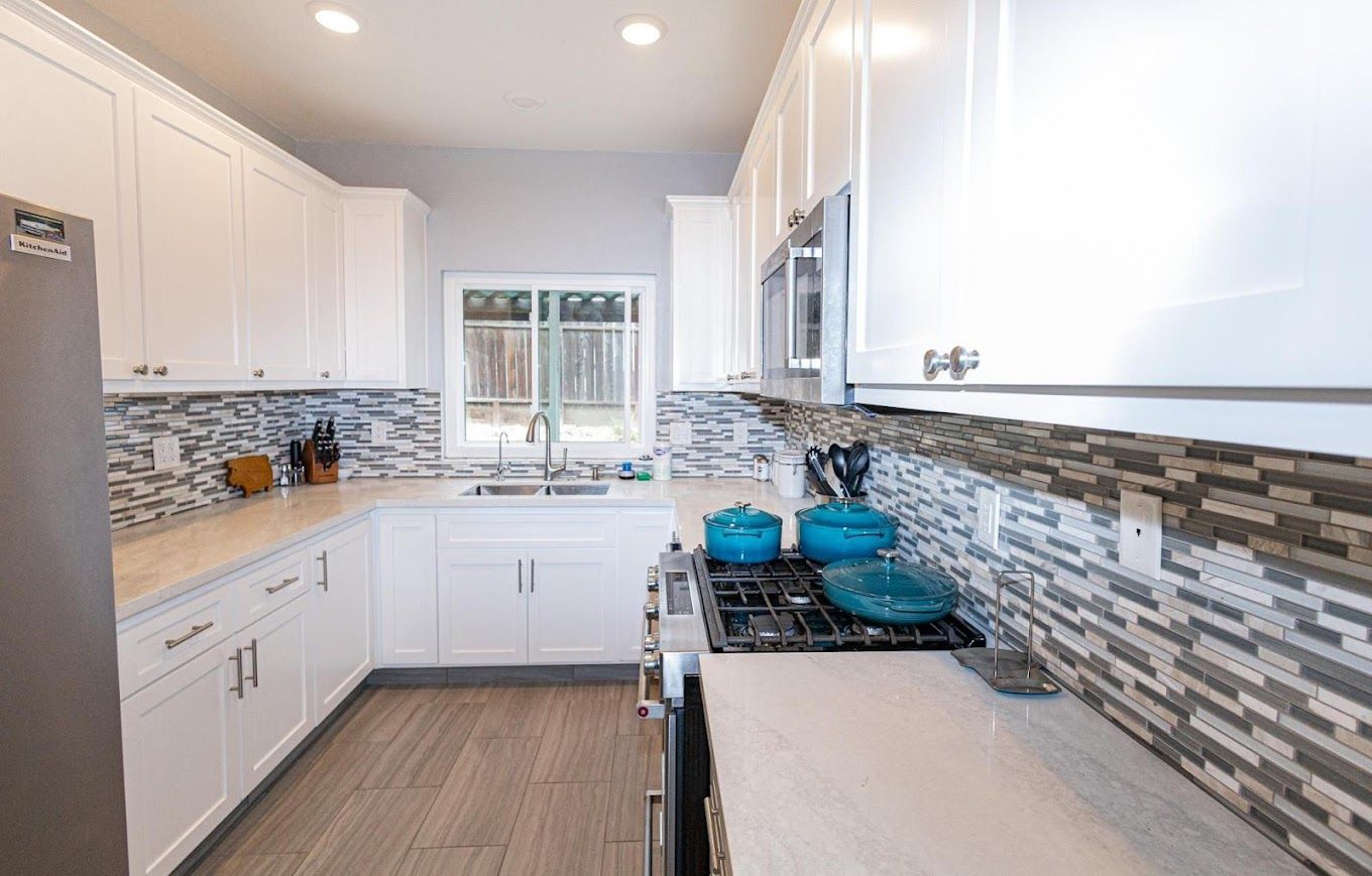 A kitchen with white cabinets , a stove , a refrigerator , and a window.