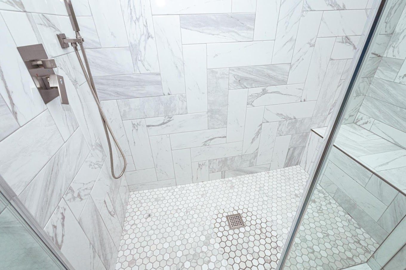 A walk in shower with marble tiles and a glass door.