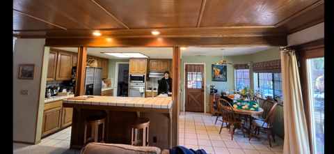 Interior view of a kitchen and dining area. Warm-toned wooden ceiling and cabinetry, with a person standing in the kitchen.