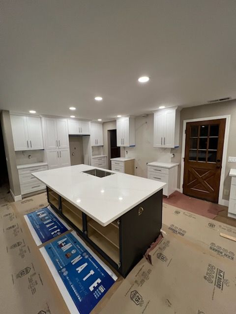 A newly renovated kitchen with white cabinets and a large dark-colored island with a white countertop. The island has an inset cooktop.