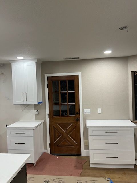 Kitchen with white cabinets, quartz countertops, a dark wooden door with glass panes, and beige walls.