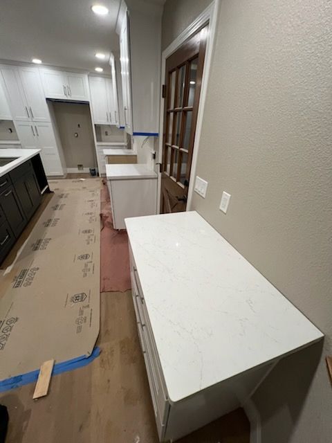 A kitchen under construction with white cabinets, countertops, and a dark wood door. Cardboard covers the floor.