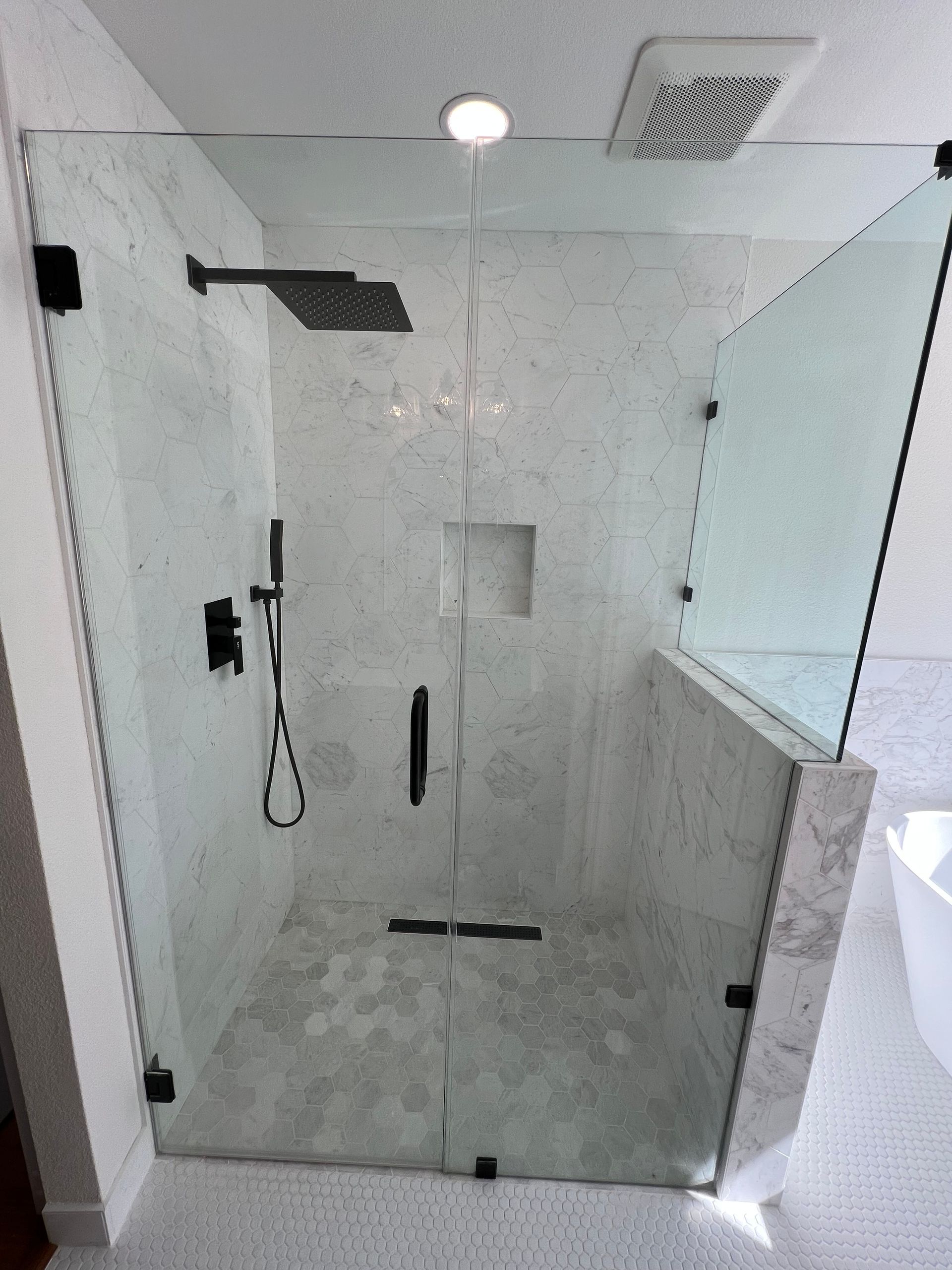 Modern shower with a glass enclosure and black hardware against a marble-tiled backdrop. Includes a rain shower head and hand shower.
