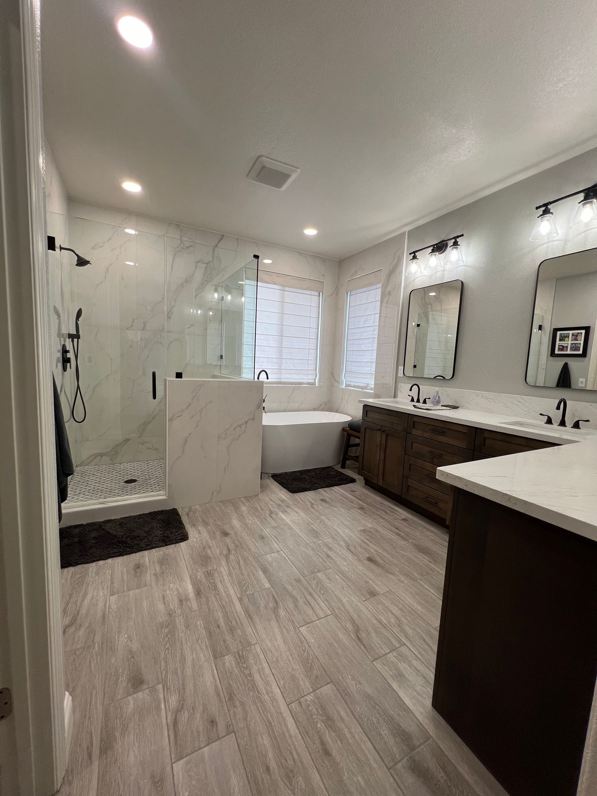 Spacious modern bathroom with marble shower, wood vanity, and soaking tub.  Neutral tones and good lighting.