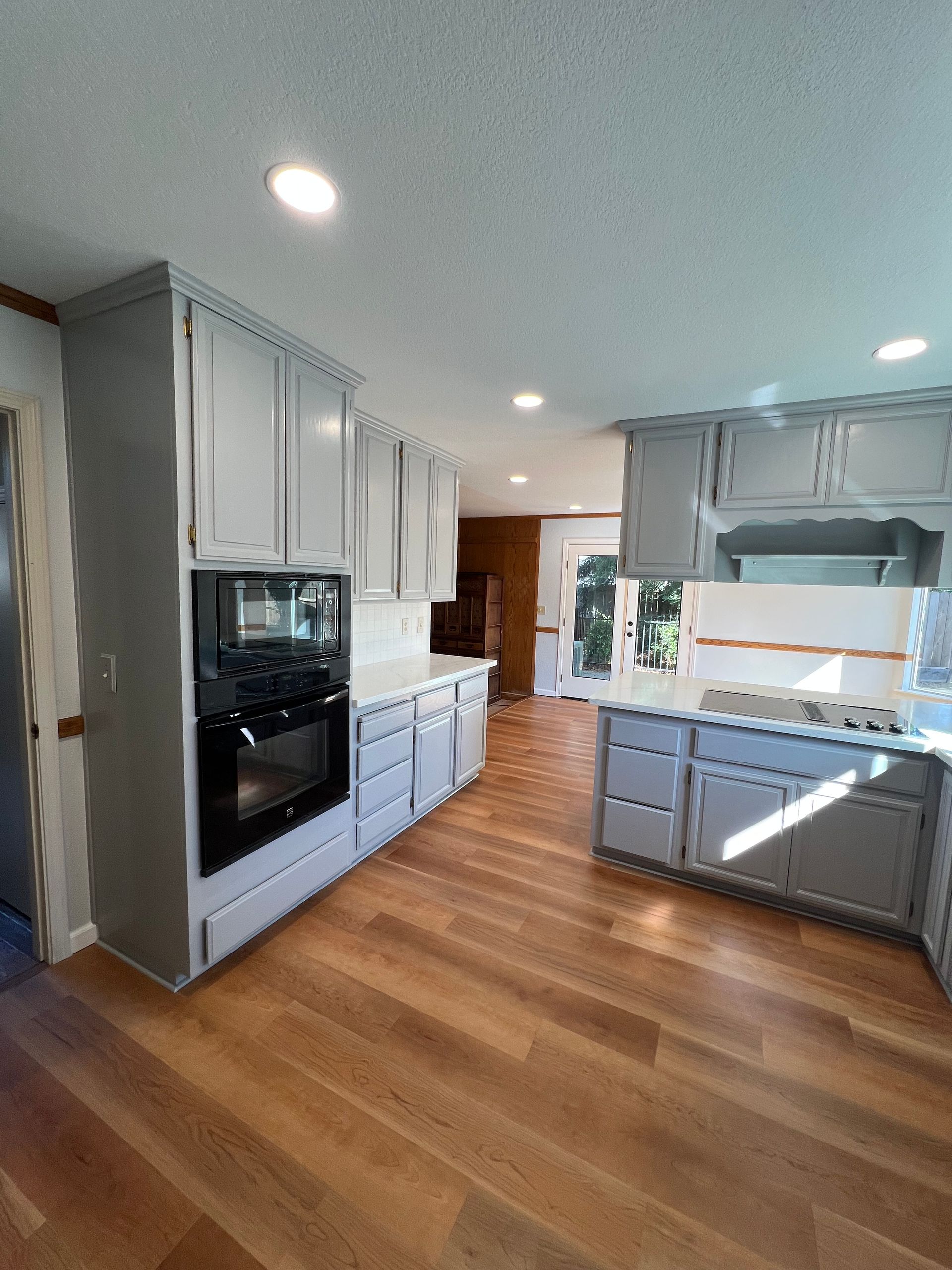 Gray cabinets and white countertops in a kitchen with hardwood floors. An oven is built into the cabinetry.