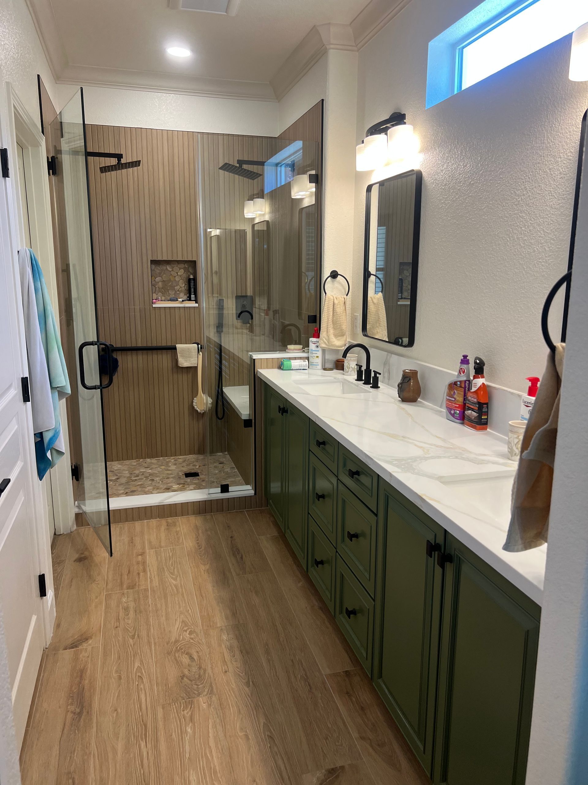 Bathroom with wood-look floor, green cabinets, white countertops, a glass shower, and a double vanity.