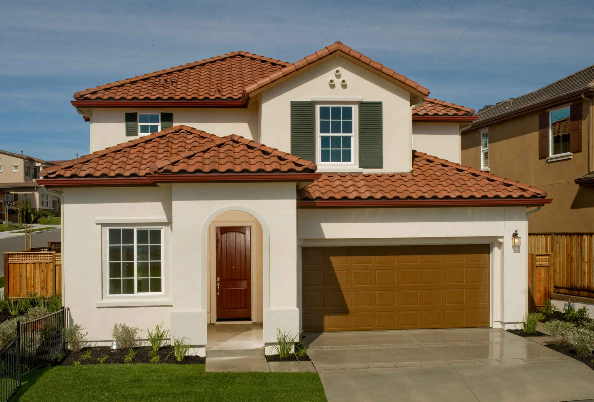 A white house with a red tile roof and a brown garage door
