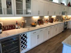 A kitchen with white cabinets , granite counter tops , a wine cooler and a wine rack.