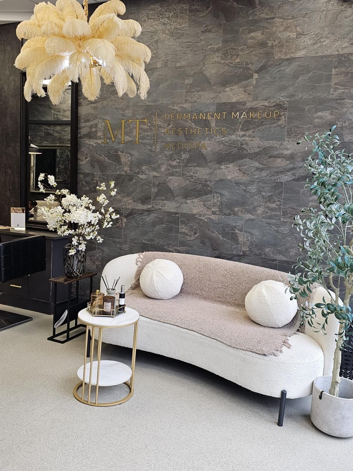 Cozy waiting area with white sofa, round pillows, and side table. Features a statement light and dark gray stone wall.