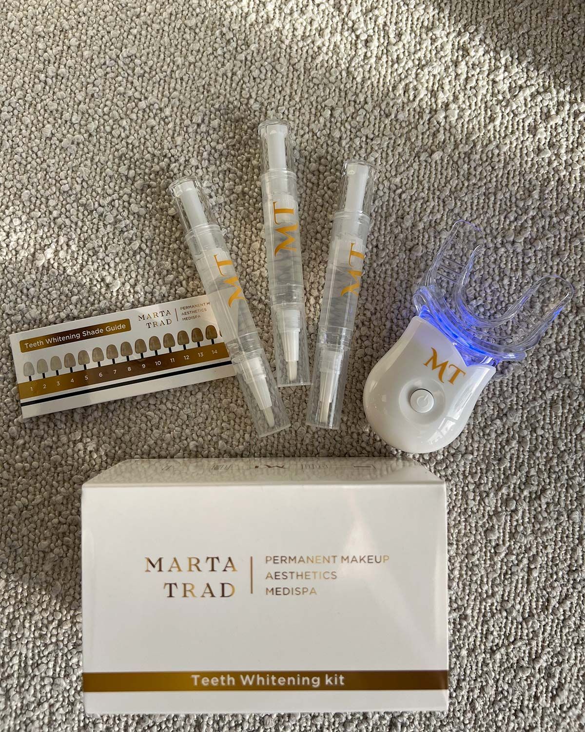 Teeth whitening kit. Includes syringes, shade guide, LED light, and box on a grey surface.