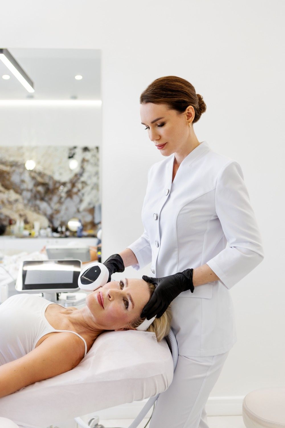 Woman receiving facial treatment in a clinic; a medical professional holds a device to her face.
