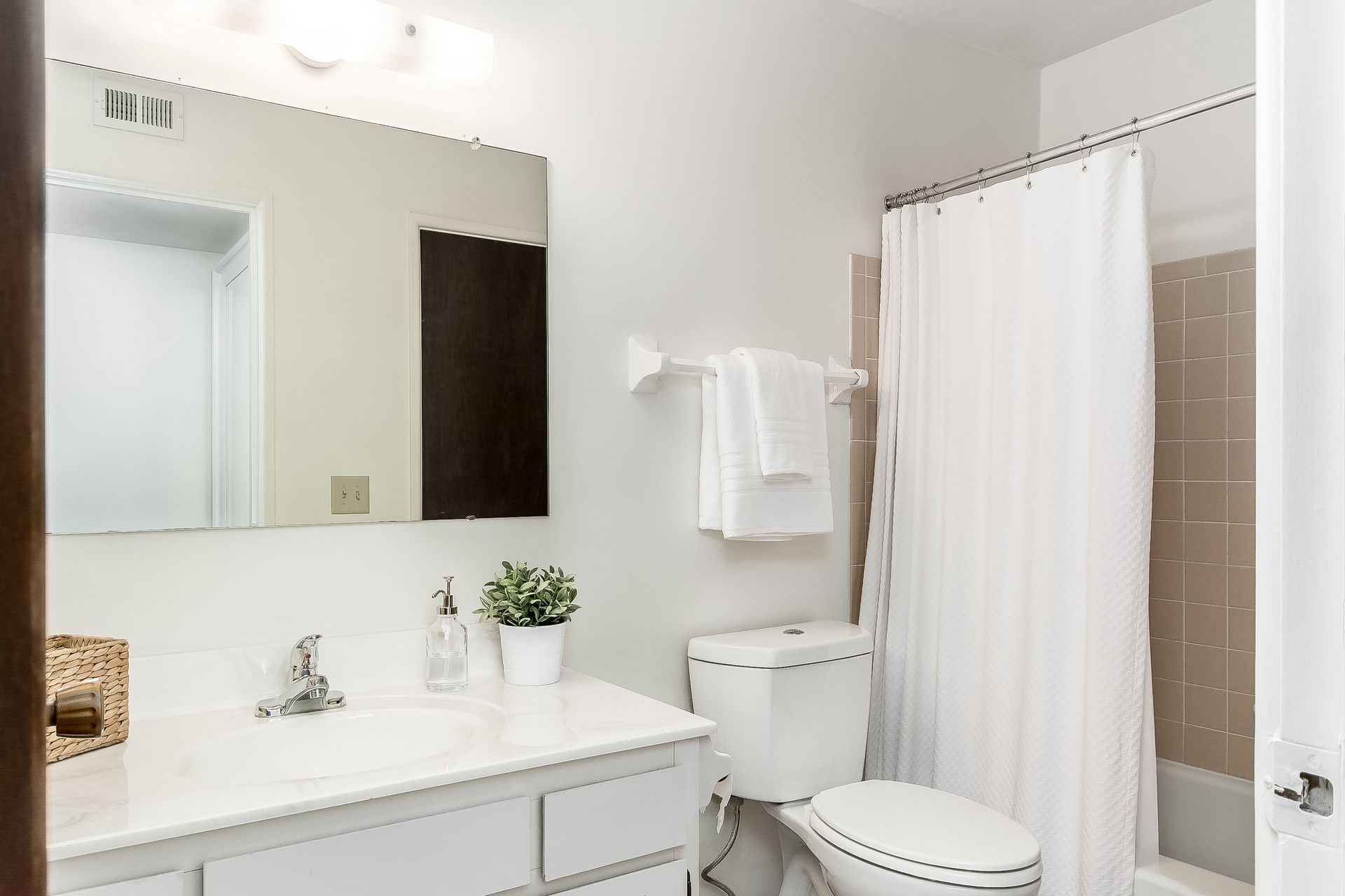 A bathroom with a toilet , sink , mirror and shower curtain.