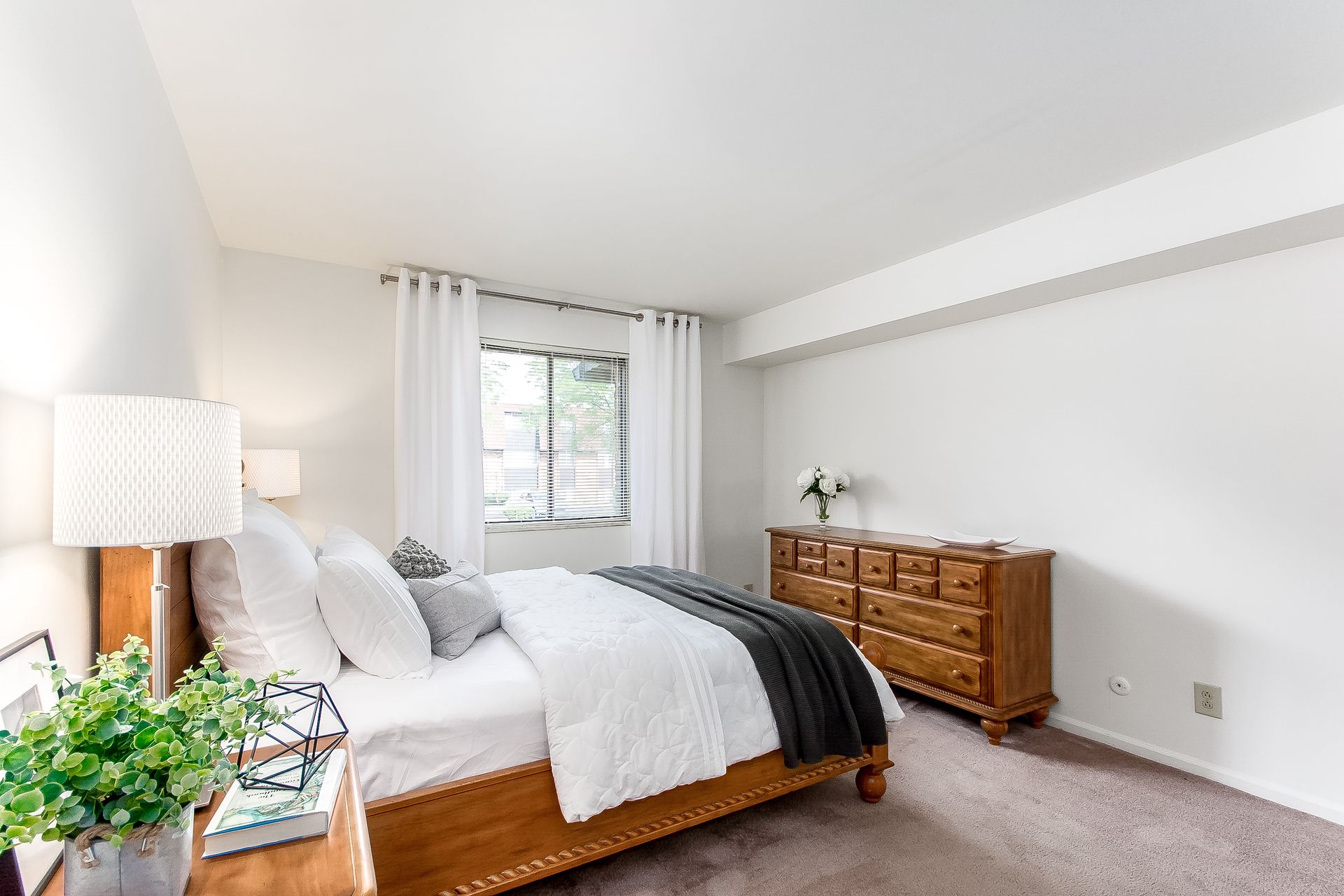 A bedroom with a bed , dresser , lamp and window.
