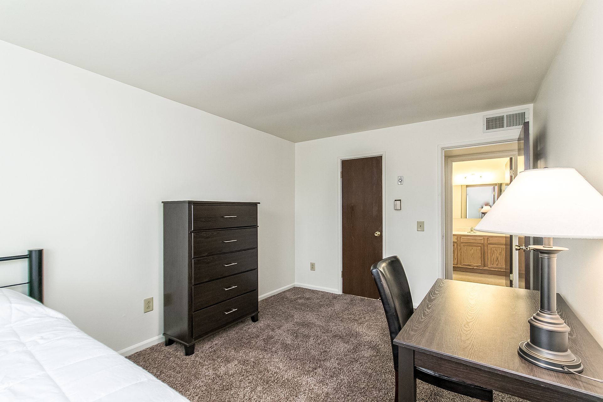 A bedroom with a bed , desk , lamp and dresser.