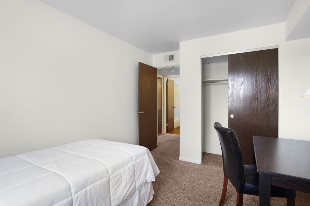 A bedroom with a bed , desk , chair and closet.