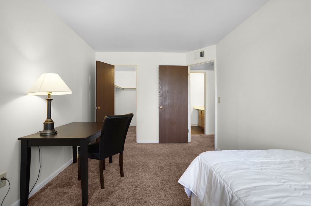 A bedroom with a bed , desk , chair and lamp