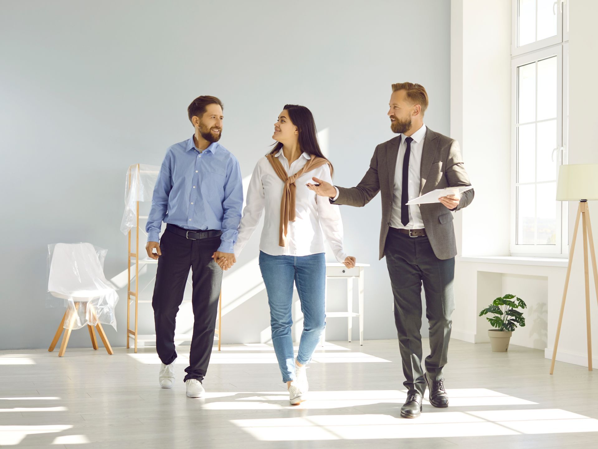 Real estate agent showing a couple a new home with light blue walls and minimal furniture.