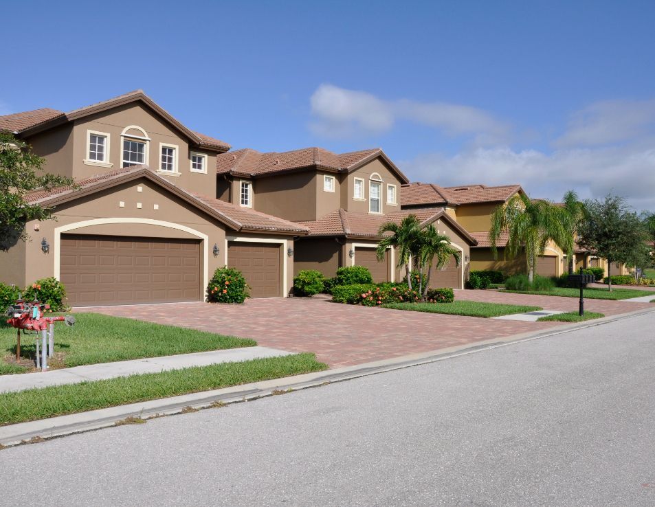 Row of beige stucco houses with brown tile roofs and brick driveways on a sunny day.
