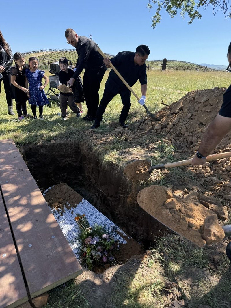 Mourners lower a coffin into a grave at a graveside burial outdoors.