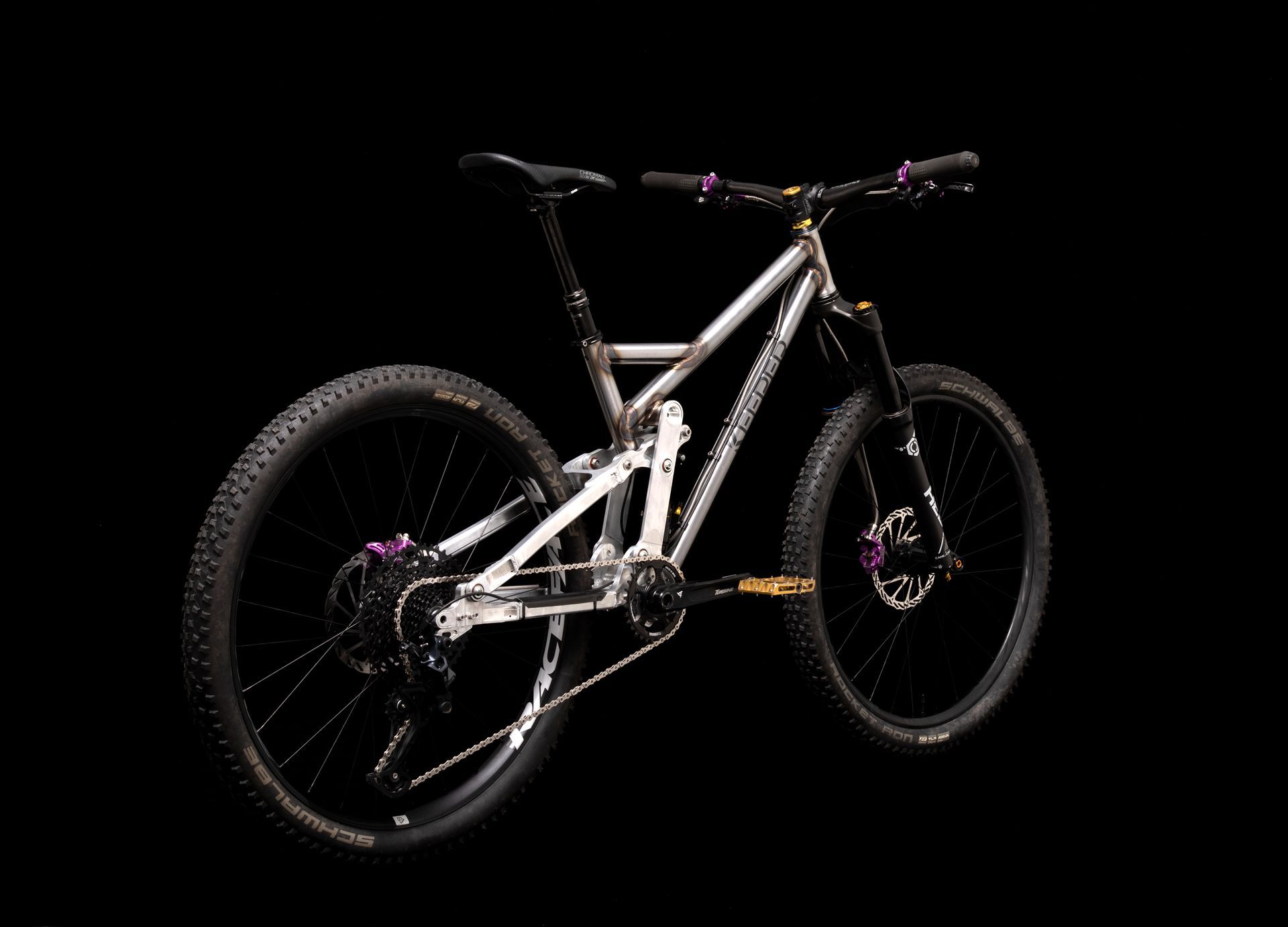 A vintage silver bicycle with red handlebars and light brown tires on a black background.