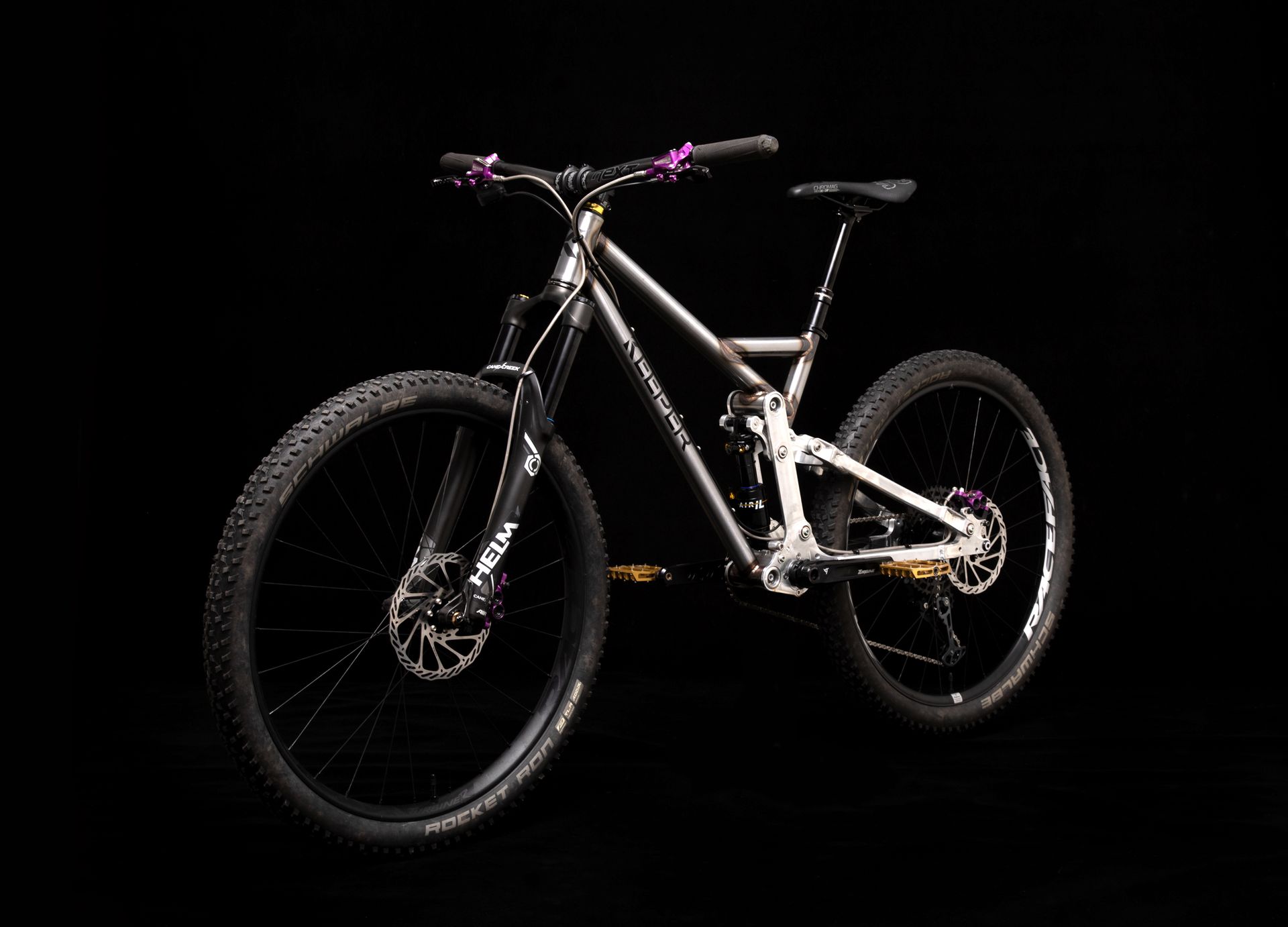 Mountain bike with black tires, purple accents, and a silver frame against a black backdrop.