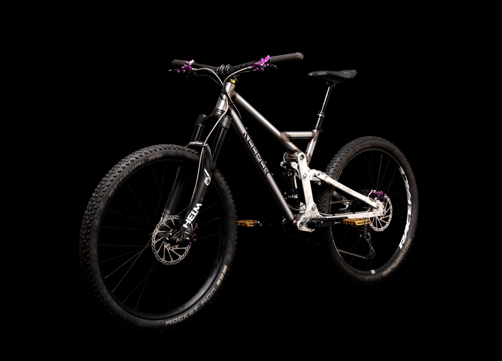 Mountain bike with black tires, purple accents, and a silver frame against a black backdrop.