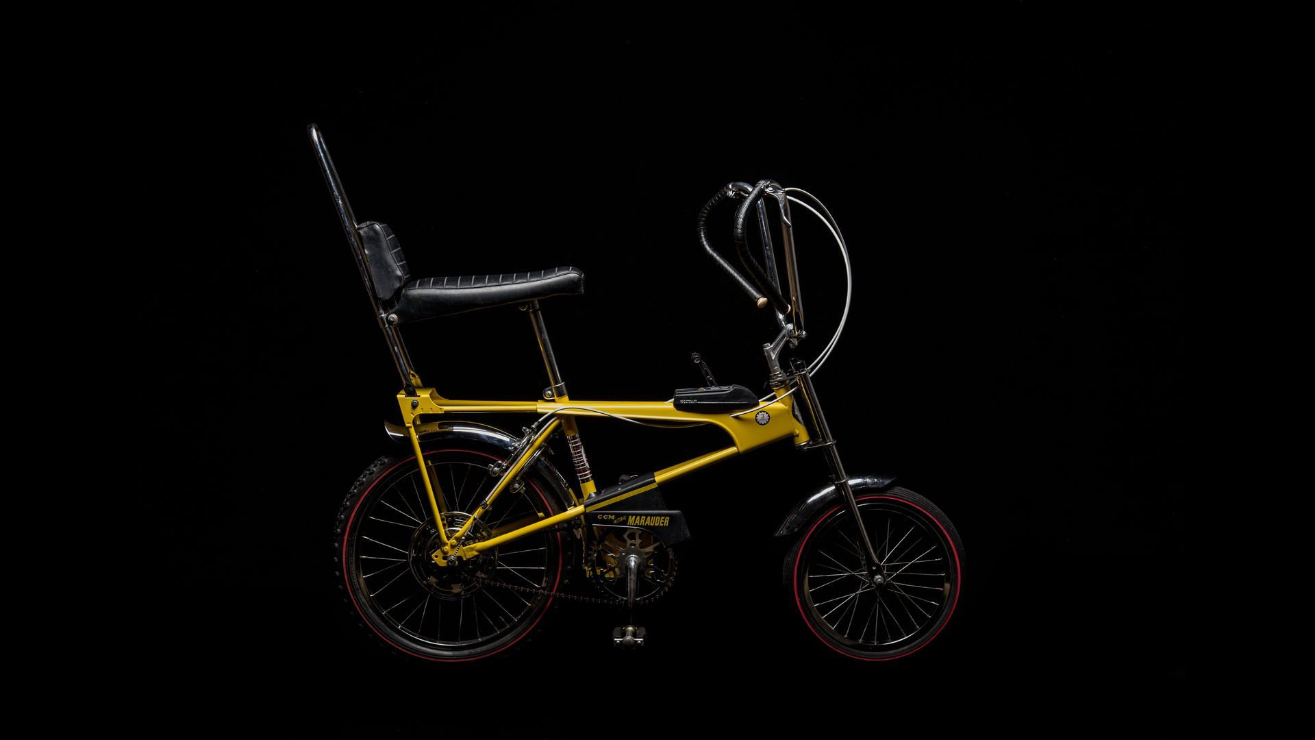 Yellow and black banana seat bike against a black background.