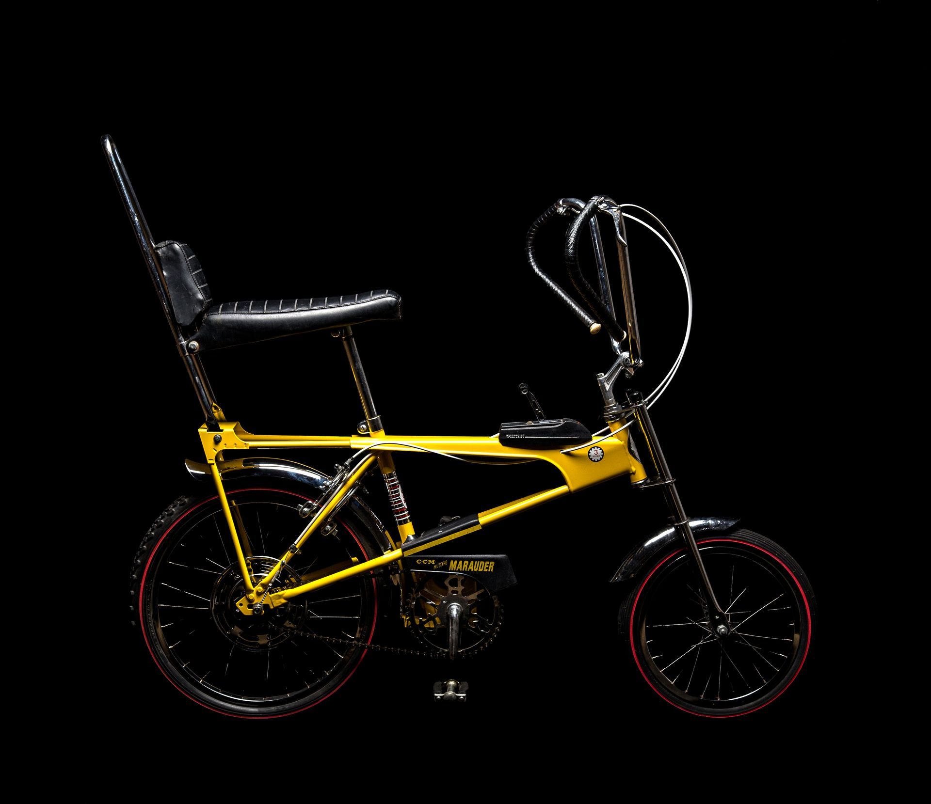 Yellow and black banana seat bike against a black background.