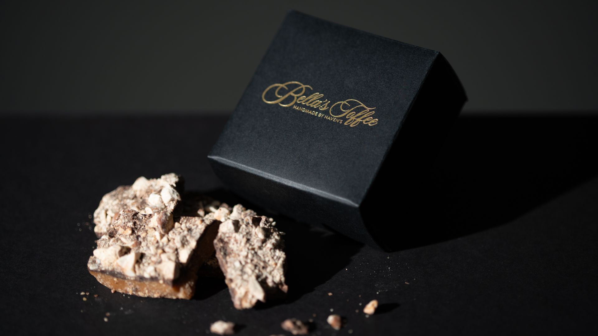 Black jewelry box beside a rough, pale gemstone on a dark surface with scattered crumbs
