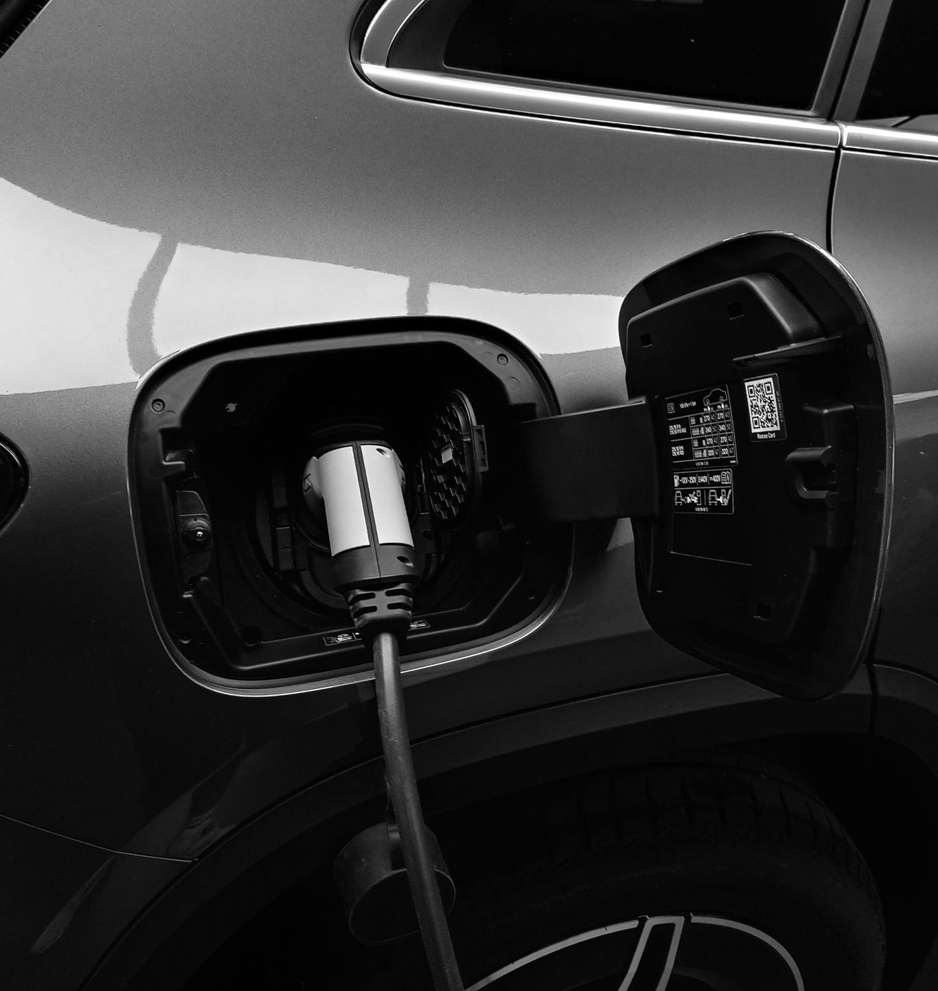 a black and white photo of an electric car being charged.