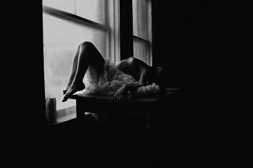 Woman in white dress reclines on windowsill, arms and legs dangling; black and white photo.