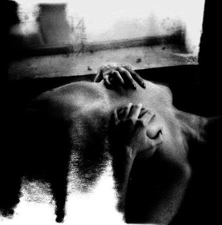 A person lying down, hands on chest, in a dark space, high-contrast black and white.