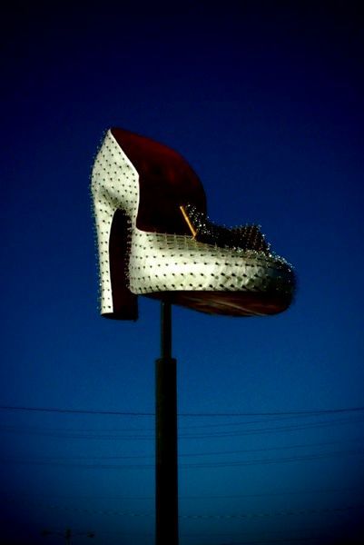 A tall, illuminated sign of a high-heeled shoe against a dark blue sky.