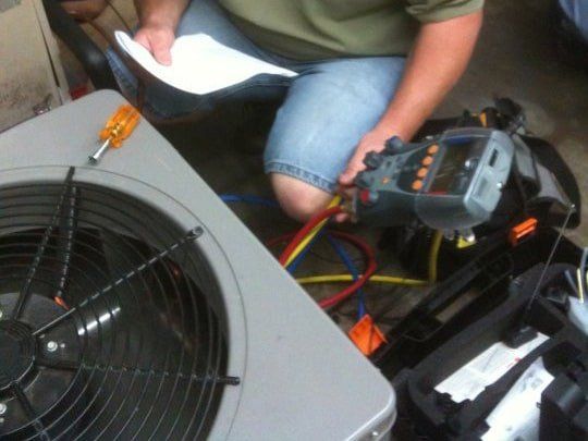 A man is kneeling down next to an air conditioner