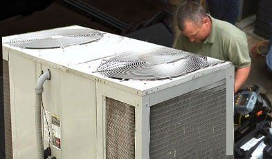A man in a green shirt is working on an air conditioner.