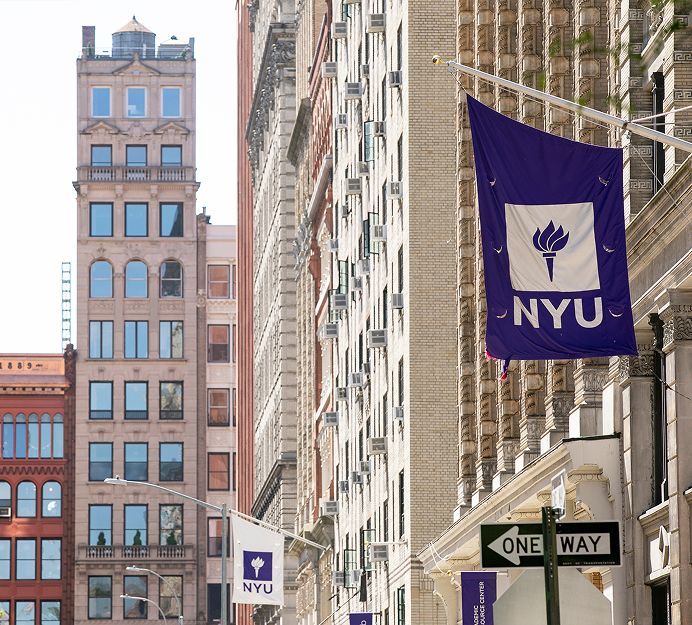 Street view of NYU buildings in New York City with purple flags and signs, featuring a one-way street sign.