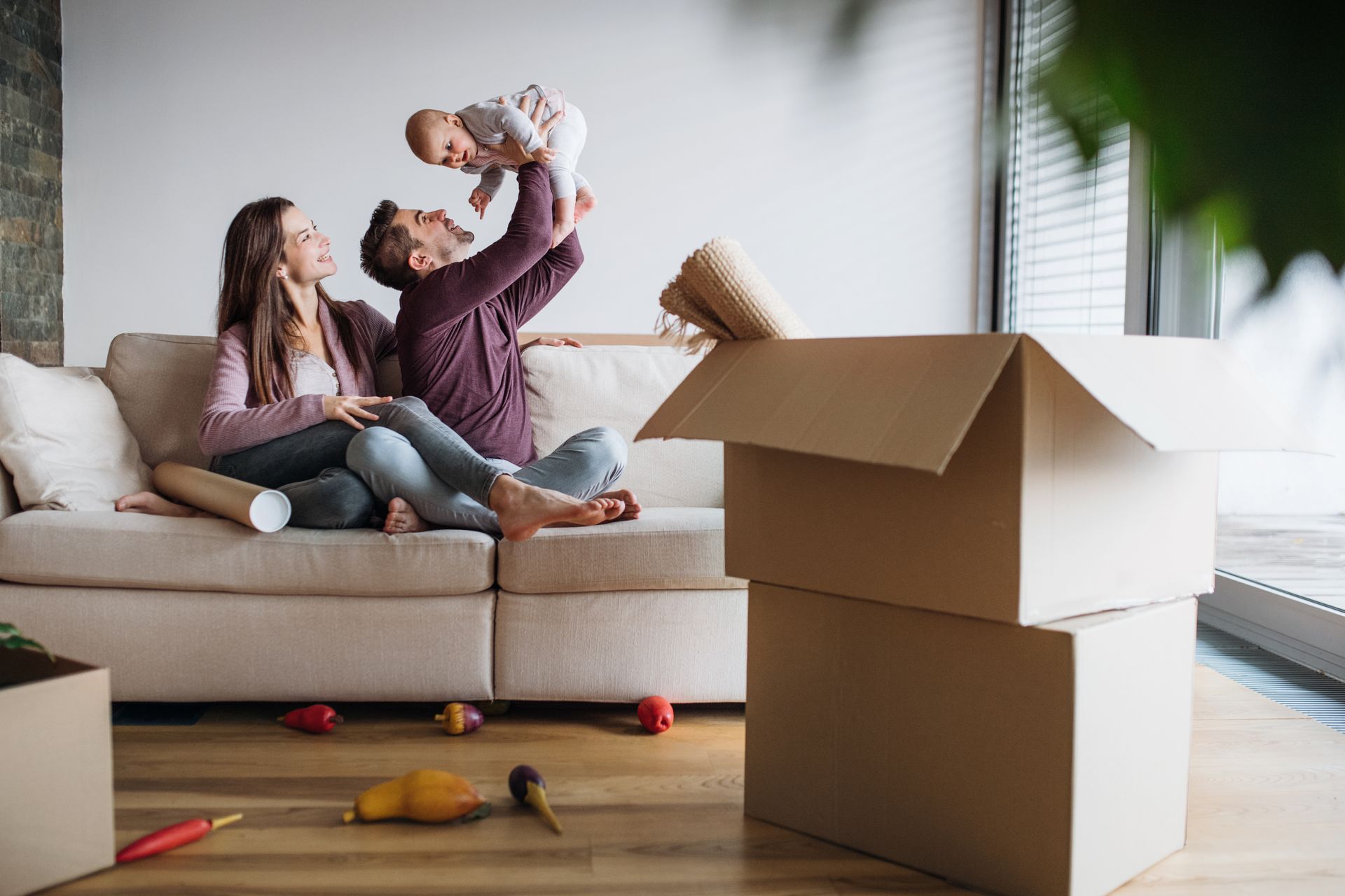 Family celebrating in new home with baby, cardboard boxes and unpacked items.