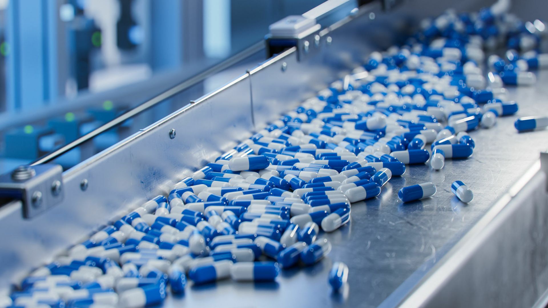 Blue and white capsules on a conveyor belt in a pharmaceutical factory.