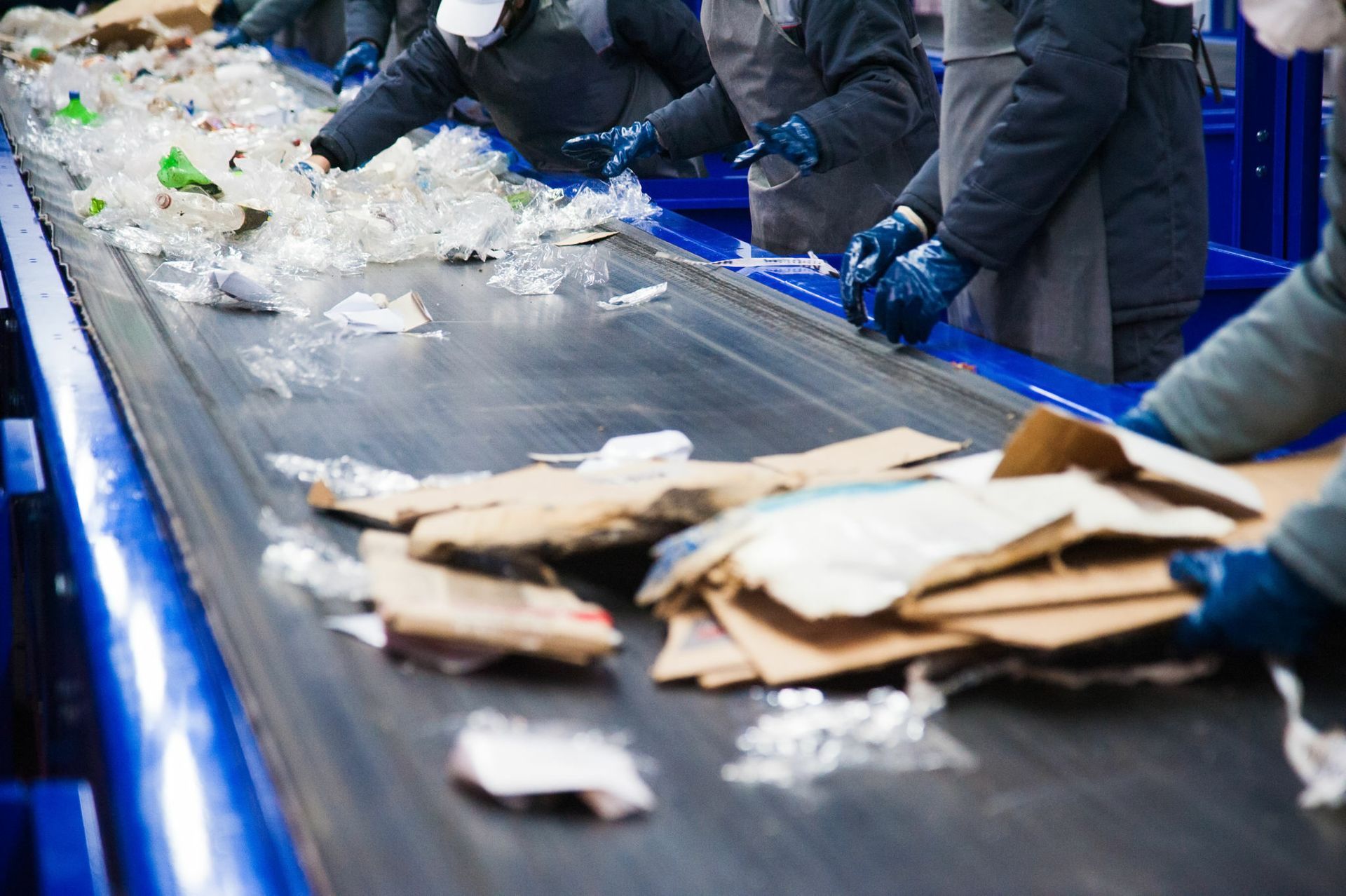 Workers sorting recyclables (plastic and cardboard) on a conveyor belt in a recycling facility.