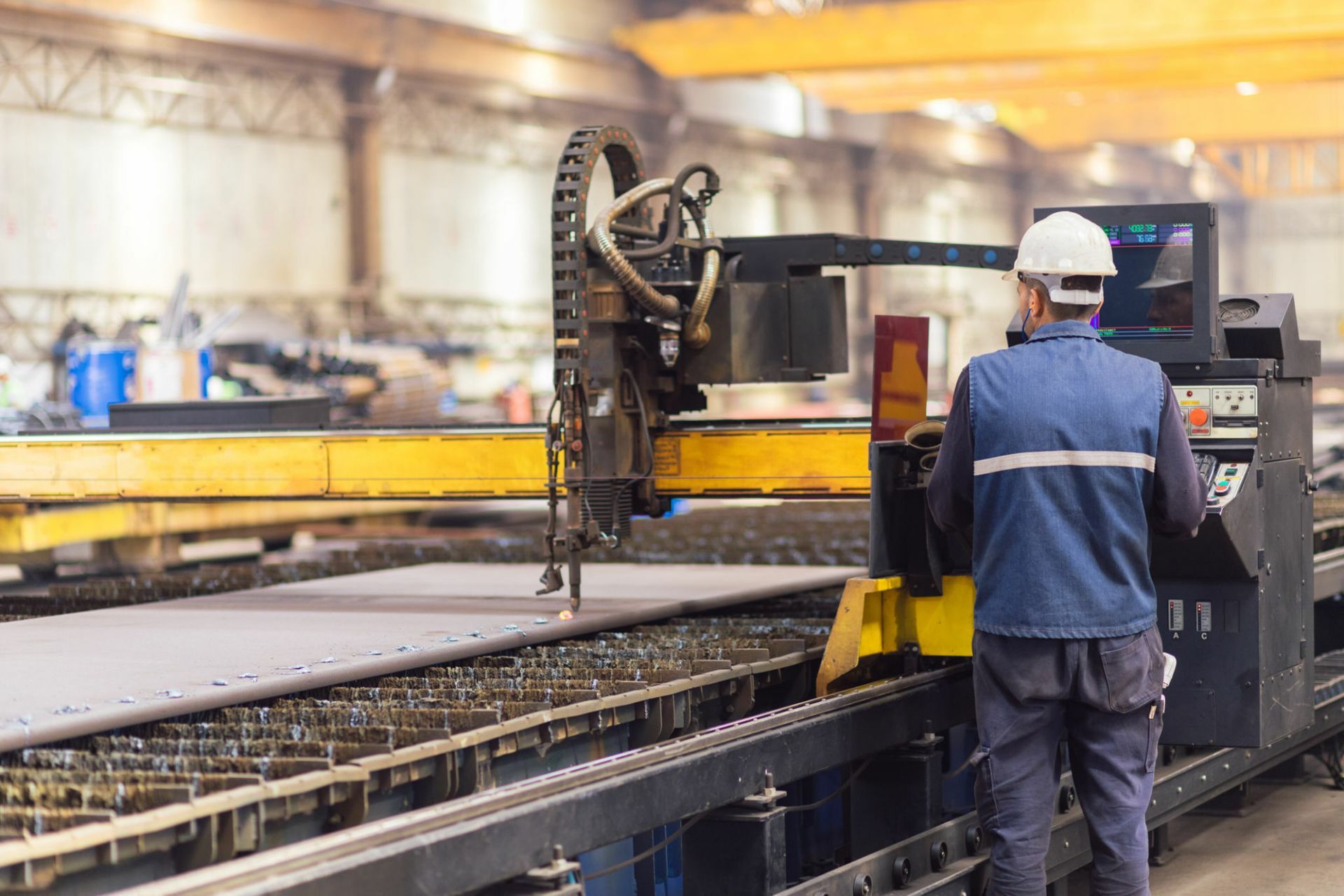A worker in a hardhat operates a metal cutting machine in a factory.