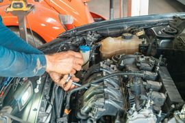 Mechanic working on a car engine in a garage; uses a wrench.